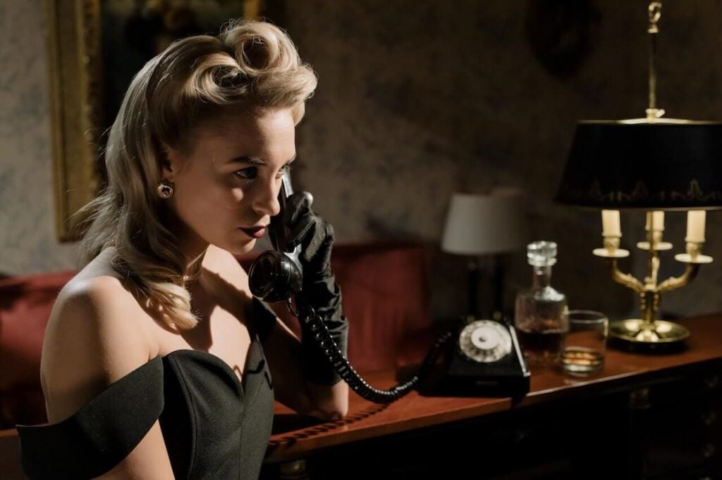 A woman dressed in 1950s-era clothing answers an antique phone